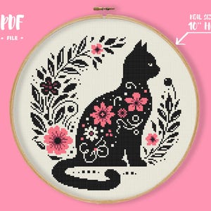 May include: Cross-stitch pattern featuring a black cat silhouette adorned with pink and white floral designs, surrounded by a floral wreath. The design is set within a 10-inch embroidery hoop, with the text "PDF FILE".