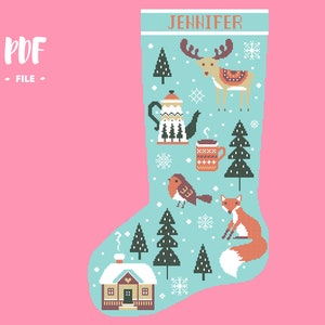 May include: A light blue Christmas stocking cross-stitch pattern featuring the name JENNIFER at the top. The design includes a reindeer, a teapot, a mug, a bird, a fox, pine trees, snowflakes, and a small house with a chimney on a pink background.