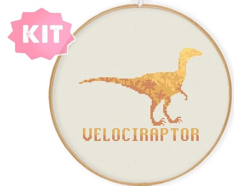 May include: Cross stitch kit featuring a yellow Velociraptor dinosaur with the text "Velociraptor" underneath. The kit is in a round wooden embroidery hoop.