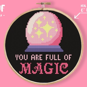 May include: Cross-stitch embroidery in a 6-inch hoop. The design features a pink crystal ball with yellow stars on a black background. The text "YOU ARE FULL OF MAGIC" is stitched in pink.