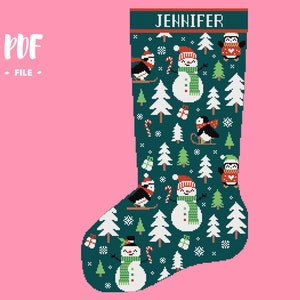 Op de afbeelding: Een donkergroene kerstsok met een kruissteekpatroon van sneeuwpoppen, pinguïns en witte dennenbomen. De boord bovenaan toont de naam JENNIFER in witte hoofdletters. Het ontwerp bevat kleine cadeautjes en zuurstokken als decoratieve elementen.