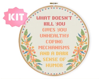 May include: A cross-stitch embroidery kit featuring a white hoop with a beige fabric background. The fabric has a cross-stitch design of a floral border and the text "WHAT DOESN'T KILL YOU GIVES YOU UNHEALTHY COPING MECHANISMS AND A DARK SENSE OF HUMOR".