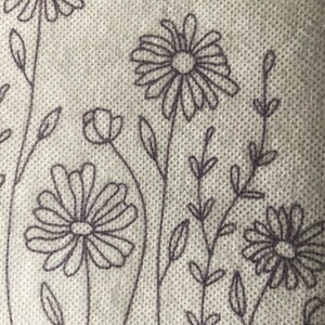 May include: A white fabric with a repeating pattern of black embroidered flowers and leaves. The flowers have a simple design with multiple petals.
