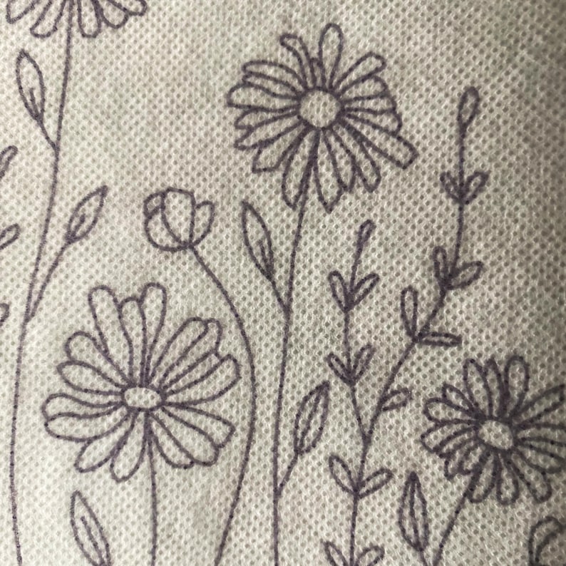 May include: A white fabric with a repeating pattern of black embroidered flowers and leaves. The flowers have a simple design with multiple petals.