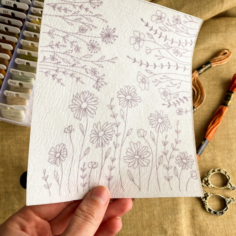 May include: A white fabric with a printed design of flowers and leaves. The design is in a light gray color.
