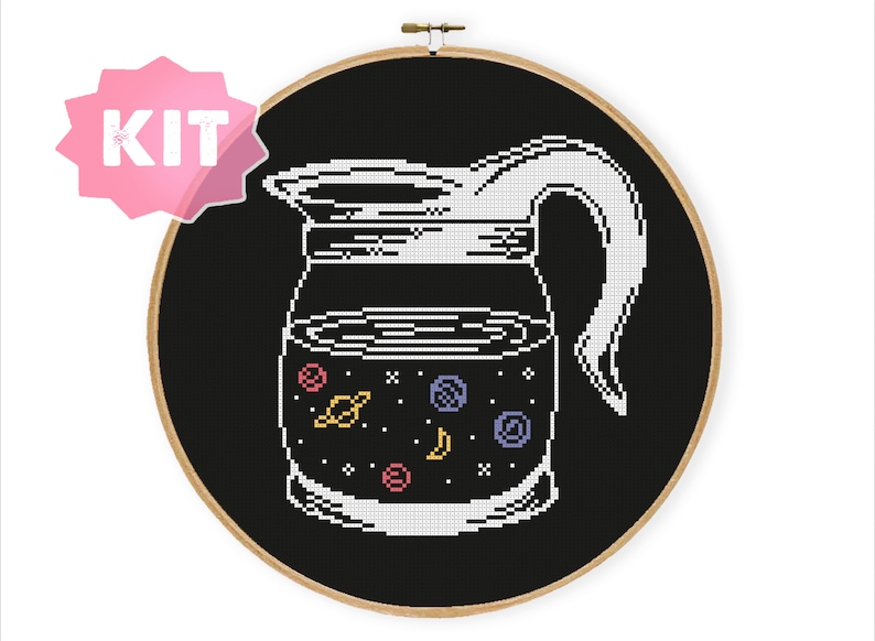 May include: Cross-stitch kit featuring a coffee pot design with a space-themed interior. The pot is white, set against a black background, and framed in a wooden hoop. The interior of the pot includes planets, stars, and a crescent moon.