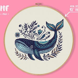 May include: A cross-stitch pattern of a whale with floral accents in a wooden hoop. The whale is navy blue and light blue, with a decorative design. The text "PDF - FILE" is in the upper left corner. The hoop size is 30 cm.