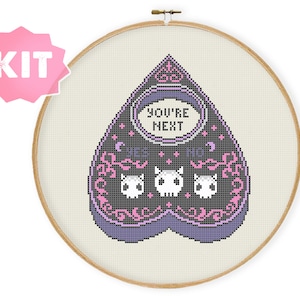 May include: A black and purple heart-shaped Ouija board with the text "You're Next" and three white skulls. The board has pink and white accents.