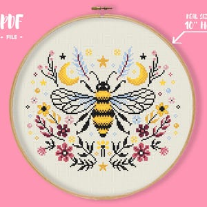 May include: A cross-stitch pattern featuring a bee with yellow and black stripes, surrounded by floral and celestial elements. The design includes moons, stars, and flowers in various colors. The text "REAL SIZE IN 10" HOOP" is visible.