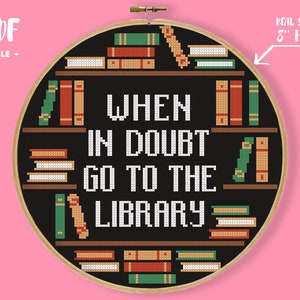 Puede incluir: Patrón de punto de cruz en blanco y negro en un aro de bordado de 20 cm. El patrón presenta una estantería con libros y el texto "WHEN IN DOUBT GO TO THE LIBRARY".