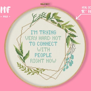 Puede incluir: Patrón de punto de cruz con una corona de flores, un marco geométrico dorado y el texto "Estoy intentando muy duro no conectar con la gente ahora mismo". El patrón está diseñado para un aro de 10 pulgadas.