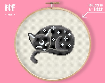 May include: A black cat with white stars on its fur is curled up in a 6-inch embroidery hoop. The cat is sleeping with its eyes closed. The hoop is on a pink background.