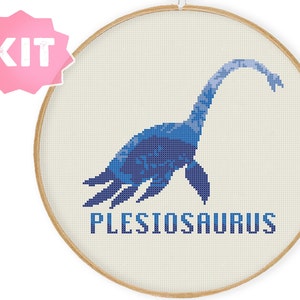 May include: A cross-stitch kit featuring a blue plesiosaur with the text "PLESIOSAURUS" underneath. The kit is displayed in a wooden embroidery hoop.