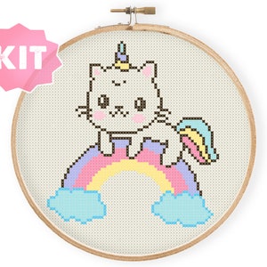 Puede incluir: Un kit de punto de cruz con un gato blanco con un cuerno de arcoíris sentado en un arcoíris con nubes. El kit incluye todos los materiales necesarios para completar el proyecto.