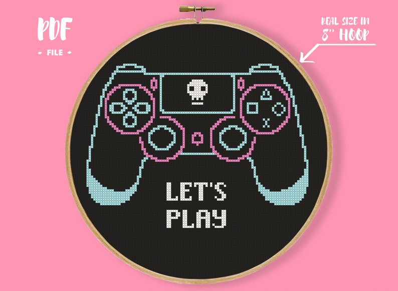 以下が含まれることがあります： 黒い背景に、水色とピンクのゲームコントローラーをあしらったクロスステッチのデザイン。「LET'S PLAY」の文字がコントローラーの下にあります。デザインは20cmのフープにセットされています。