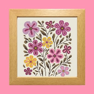 Pode incluir: Um design floral em ponto cruz emoldurado. A obra apresenta uma variedade de flores em tons de rosa, roxo e amarelo, com caules e folhas castanhos. A moldura é de madeira clara e o fundo é rosa suave.