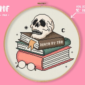 Può includere: Schema di punto croce con un teschio che indossa un cappello marrone e legge una pila di libri. Il libro in cima ha il testo "DEATH BY TBR" sulla copertina. Lo schema è progettato per un cerchio da 10 pollici.