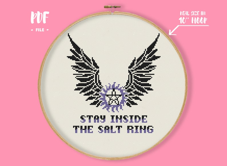 May include: Cross-stitch design in a 10-inch hoop featuring black wings above a purple pentagram and the text "STAY INSIDE THE SALT RING". The design is on a cream-colored fabric, with a wooden hoop and a pink background.