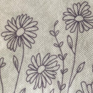 May include: A white fabric with a repeating pattern of black and white daisy flowers and stems.