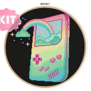 Könnte beinhalten: Ein Kreuzstich-Muster-Set mit einer pixelartigen Retro-Handheld-Spielkonsole mit einem Regenbogen und Wolken auf dem Bildschirm. Die Konsole ist von einem schwarzen Hintergrund umgeben und hat ein rosa, grünes und blaues Farbschema.