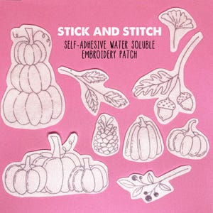 May include: A set of nine iron-on patches featuring autumnal designs. The patches include pumpkins, acorns, leaves, and a pine cone. The patches are white and are labeled "Stick and Stitch Self-Adhesive Water Soluble Embroidery Patch".