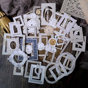 May include: A collection of vintage-style white frames with clock faces and ornate details. The frames are arranged on a gold-coloured surface.