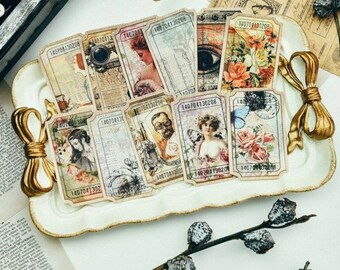 May include: A collection of vintage-style paper tickets with various illustrations, including portraits, flowers, and an eye, arranged on a white decorative tray with gold handles. Each ticket has a unique number.