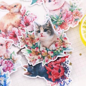 Puede incluir: Un conjunto de pegatinas coloridas con ilustraciones de acuarela de animales y flores. Las pegatinas incluyen un gato, un conejo, un cerdo y una variedad de flores.
