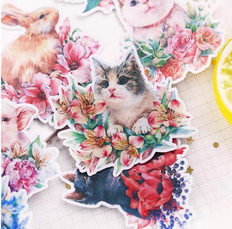 Puede incluir: Un conjunto de pegatinas coloridas con ilustraciones de acuarela de animales y flores. Las pegatinas incluyen un gato, un conejo, un cerdo y una variedad de flores.