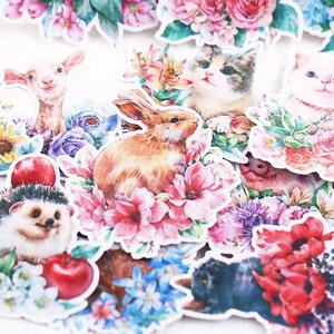 Puede incluir: Un conjunto de pegatinas coloridas con varios animales y dise&ntilde;os florales. Las pegatinas incluyen un conejo, un erizo, un gato, un cordero y un gato negro. Las pegatinas est&aacute;n rodeadas de flores en tonos de rosa, azul y rojo.