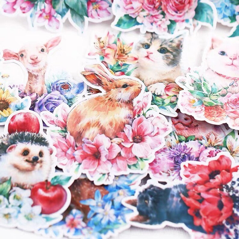 Puede incluir: Un conjunto de pegatinas coloridas con varios animales y dise&ntilde;os florales. Las pegatinas incluyen un conejo, un erizo, un gato, un cordero y un gato negro. Las pegatinas est&aacute;n rodeadas de flores en tonos de rosa, azul y rojo.
