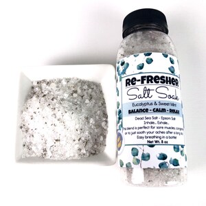 Puede incluir: Una botella de plástico transparente llena de sales de baño blancas. La botella tiene una tapa negra y una etiqueta que dice "Re-Fresher Salt Soak Eucalyptus & Sweet Mint Balance - Calm - Relax Dead Sea Salt - Epsom Salt Inhale. Exhale... This blend is perfect for sore muscles, congestion or to just soothe your aches after a long day. Easy breathing in a bottle! Net Wt. 8 oz"