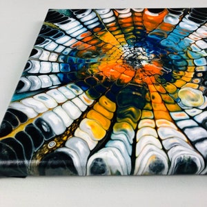Puede incluir: Pintura abstracta sobre lienzo con un patr&oacute;n de remolino de pintura negra, blanca, azul, naranja y amarilla. Los colores crean un dise&ntilde;o radial que se asemeja a una flor o una telara&ntilde;a.