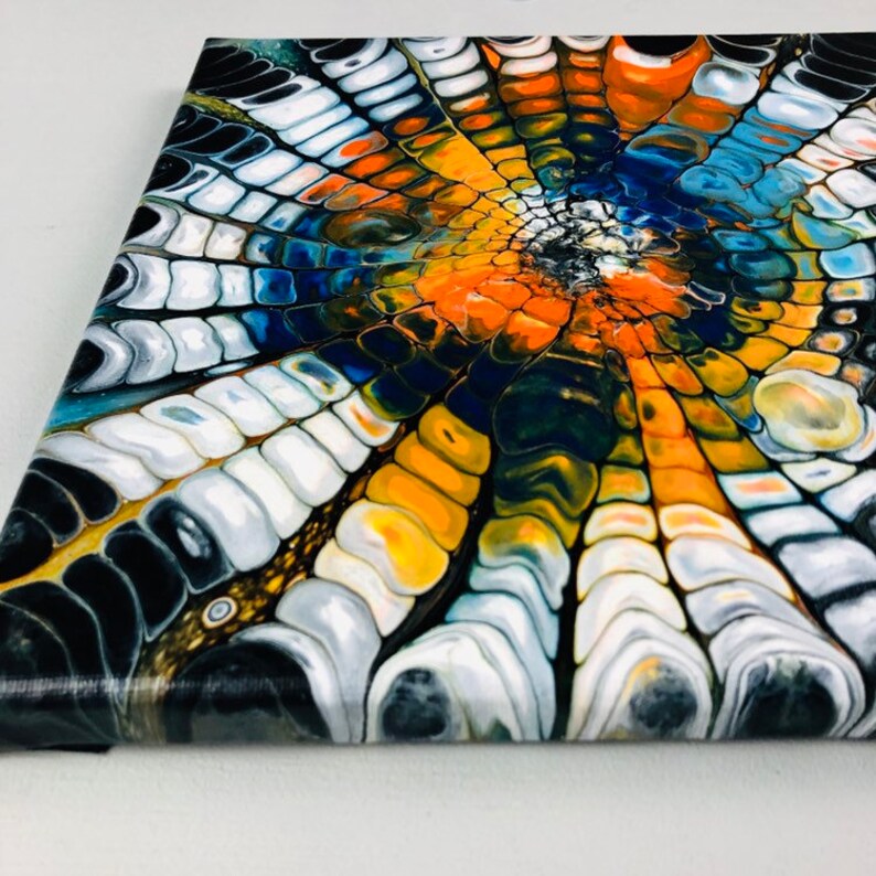 Puede incluir: Pintura abstracta sobre lienzo con un patr&oacute;n de remolino de pintura negra, blanca, azul, naranja y amarilla. Los colores crean un dise&ntilde;o radial que se asemeja a una flor o una telara&ntilde;a.