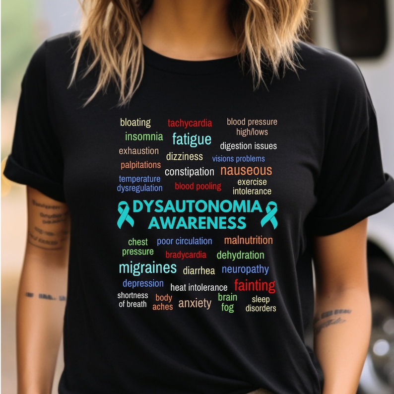 May include: A black t-shirt with a teal ribbon and the words 'DYSAUTONOMIA AWARENESS' in white. The words are surrounded by a word cloud of symptoms associated with dysautonomia, including fatigue, dizziness, nausea, chest pressure, migraines, fainting, and more.