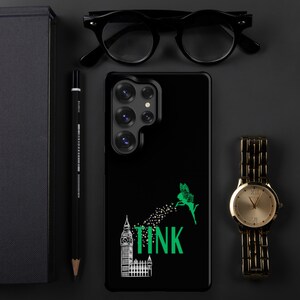 May include: Black phone case featuring a green fairy design with the word "TINK" and a Big Ben illustration. A gold wristwatch, black glasses, and a pencil are also visible.