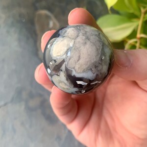 以下が含まれることがあります： 黒、白、グレーの大理石模様の研磨された球体。手で持たれており、反射する表面と複雑なデザインが特徴です。球体の直径は約5cmです。