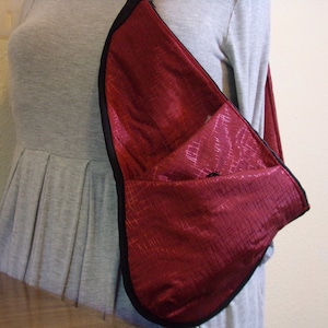 May include: A burgundy crossbody bag with a black zipper and trim. The bag is made of a textured fabric and has a single strap.