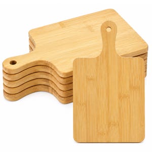 May include: A stack of six rectangular bamboo cutting boards, each featuring a light tan wood grain, rounded corners, and a handle with a circular hole at the top for hanging. The boards are arranged with one standing upright in the front.