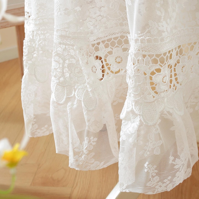 K&ouml;nnte beinhalten: Nahaufnahme eines wei&szlig;en Spitzenvorhangs mit komplizierten floralen und geometrischen Mustern. Der Vorhang hat ein mehrschichtiges Design mit gewellten Kanten und einer zarten, luftigen Textur, die eine romantische und elegante &Auml;sthetik erzeugt.