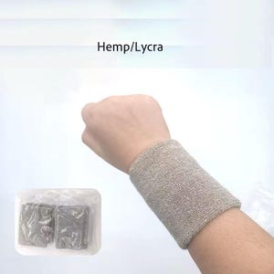 Pode incluir: Uma pulseira bege feita de cânhamo/lycra é usada no pulso de uma pessoa. A pulseira é de cor sólida e parece ser feita de um material macio e absorvente. Duas pulseiras adicionais são embaladas em um recipiente de plástico transparente.