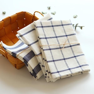 May include: A stack of four white kitchen towels with blue checkered patterns. The towels are tied together with twine and are folded neatly.