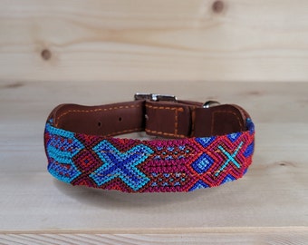 May include: A colorful dog collar with a geometric pattern in shades of red, blue, and turquoise. The collar is made of woven fabric and has a brown leather base.