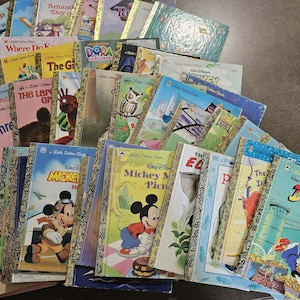 May include: A collection of vintage children's books, including titles like "Donald Duck", "Mickey Mouse", and "Dora the Explorer". The books feature colorful illustrations and gold-colored spines. The books are arranged in a pile, showcasing a variety of classic stories.