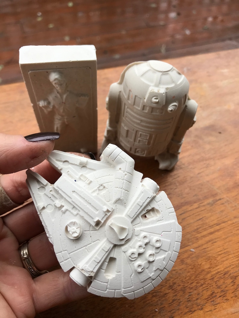K&ouml;nnte beinhalten: Hellwei&szlig;e Star Wars Figuren. Enth&auml;lt einen Millennium Falken, R2-D2 und eine Figur in Karbonit. Der Millennium Falke hat detaillierte Verkleidungen und ein zentrales Cockpit. R2-D2 ist ein runder Droide mit rechteckigen Paneelen.