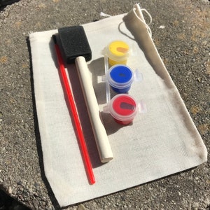 May include: A small art kit with a canvas bag, a red paintbrush, a sponge brush, and three small paint pots with yellow, blue, and red paint. The kit is designed for painting projects.
