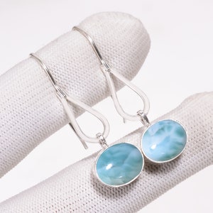 Könnte beinhalten: Ein Paar Ohrhänger mit ovalen, hellblauen Larimar-Edelsteinen in poliertem Silber. Jeder Ohrring besteht aus einem glatten, abgerundeten Stein in einer einfachen Silberfassung, der an einem tropfenförmigen Silberdraht-Haken befestigt ist.