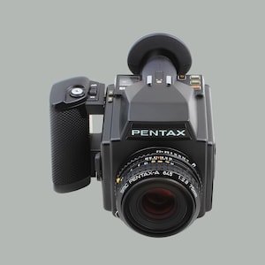 May include: Black Pentax 645 medium format film camera with a 75mm lens. The camera has a grip, viewfinder, and various dials and settings. The lens is labeled SMC Pentax-A 645 1:2.8 75mm.