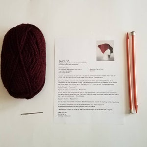 May include: A skein of burgundy yarn, two knitting needles, a yarn needle, and a printed pattern for a square hat. The pattern includes instructions and a diagram of the finished hat. The needles are approximately 13 inches long.