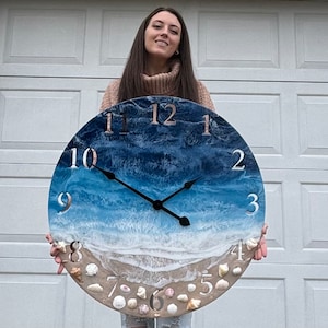 May include: A round clock with a blue and white ocean wave design. The clock face has white numbers and black hands. The clock is surrounded by a ring of seashells.